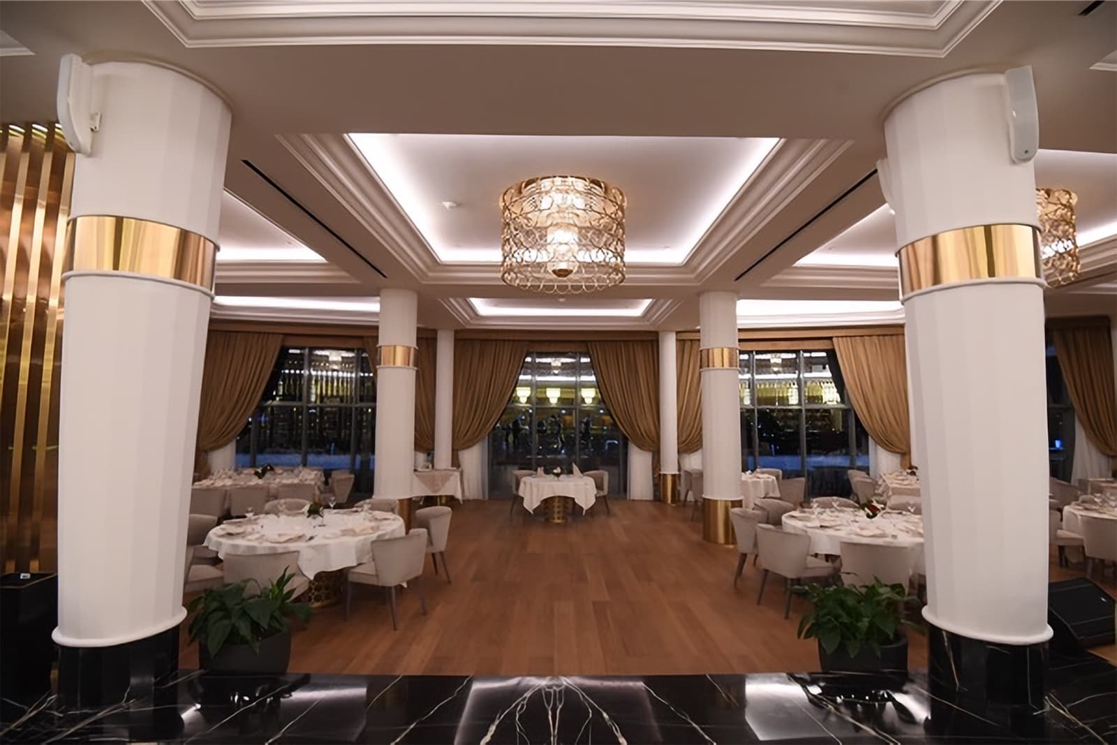 The La Martingale dining room with white columns, gold details and round tables set for dinner