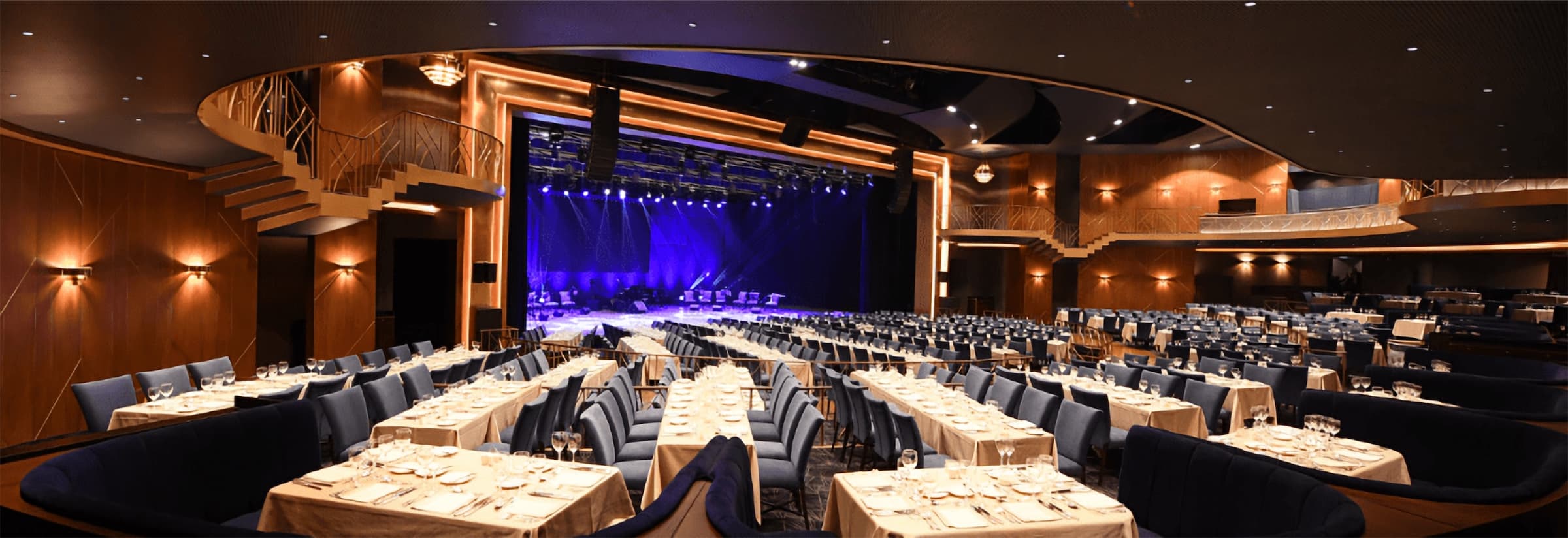 The Salle des Ambassadeurs set with white-clothed tables and blue chairs, a curved balcony above and the stage lit in blue
